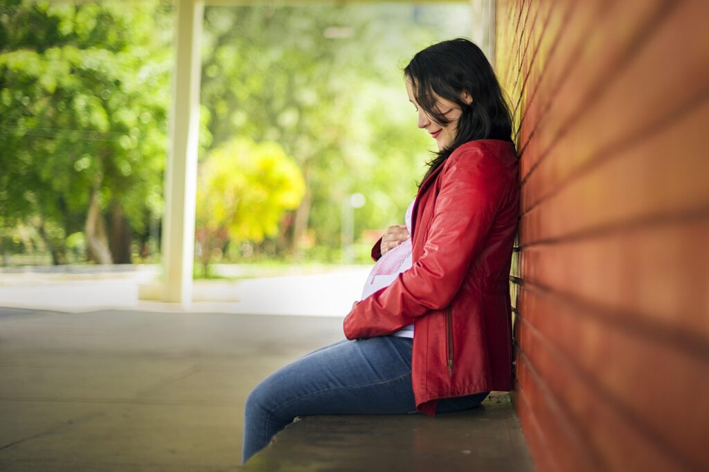 Pregnant woman sitting outdoors and smiling while touching her baby bump